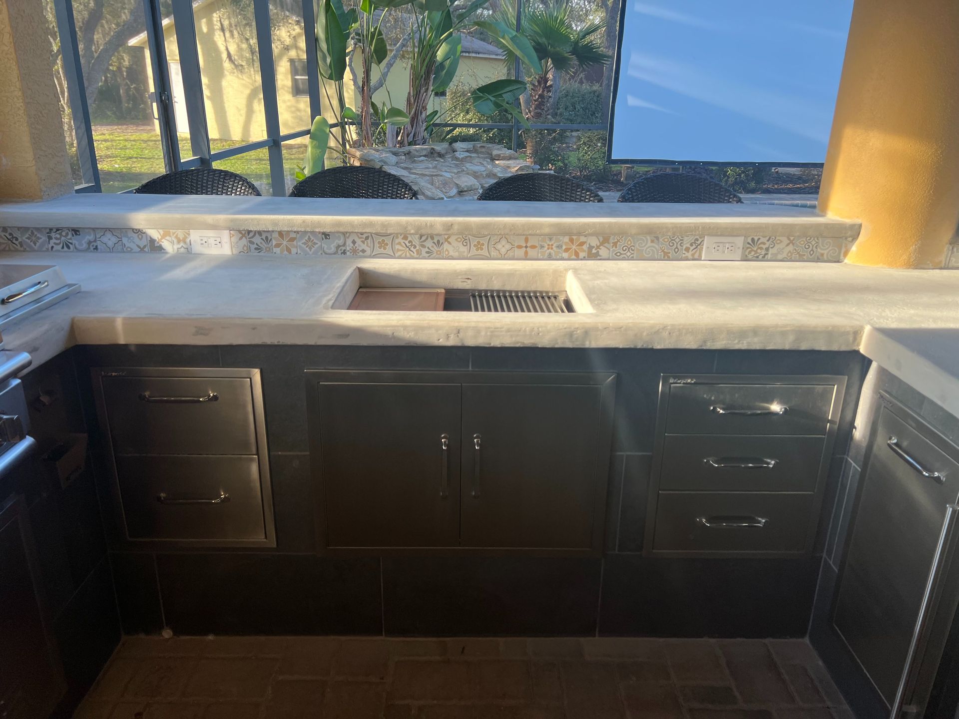 An outdoor kitchen island with a light-colored countertop, stainless steel drawers, and cabinet doors.