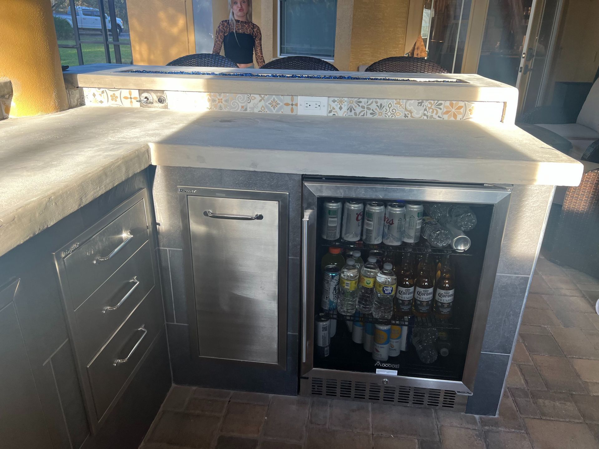 An outdoor bar area featuring a stone countertop, built-in stainless steel drawers, and a stocked glass-door refrigerator.