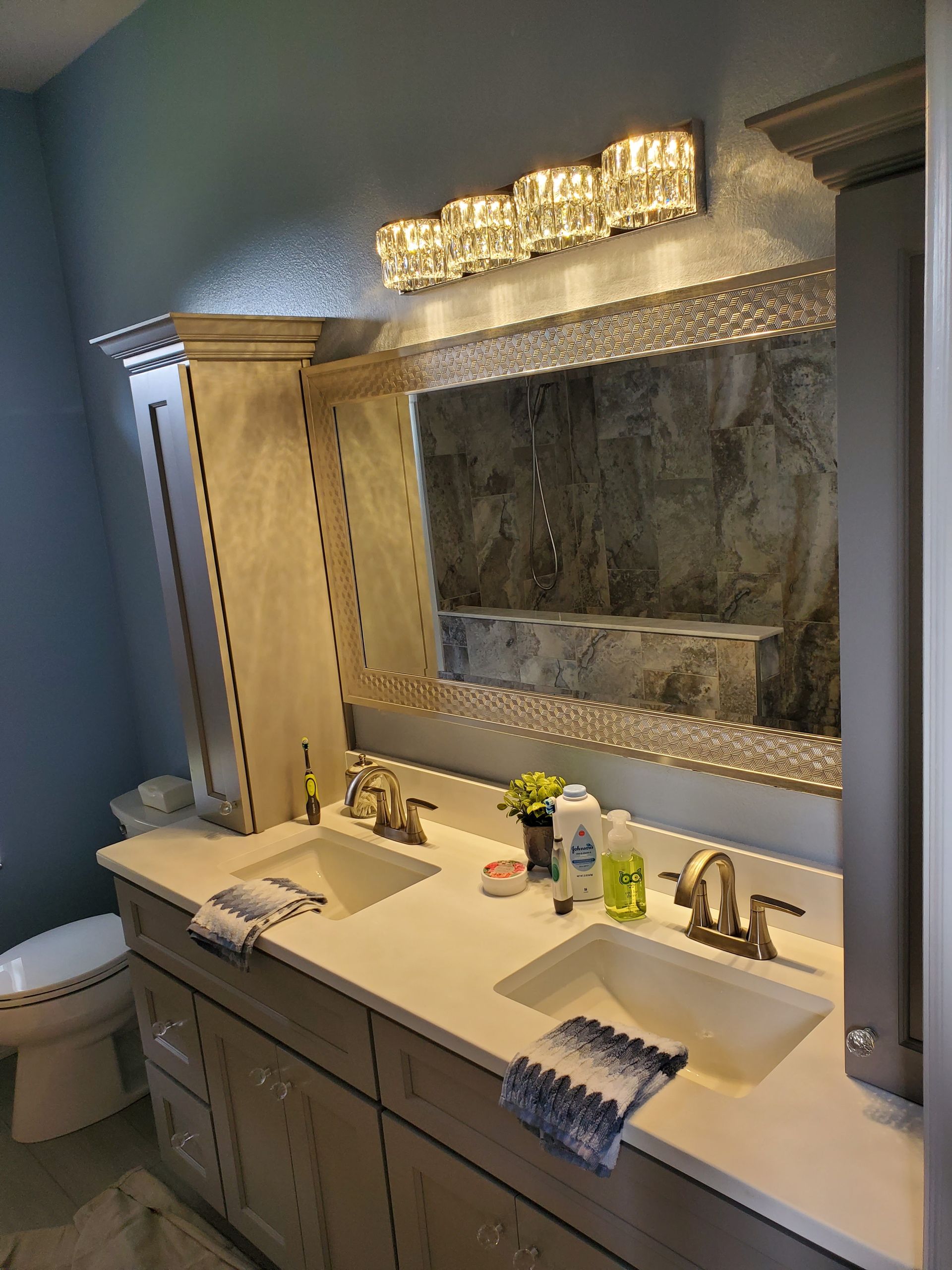 A double vanity bathroom with two sinks, a large framed mirror, vanity lights, and cabinetry against blue walls.