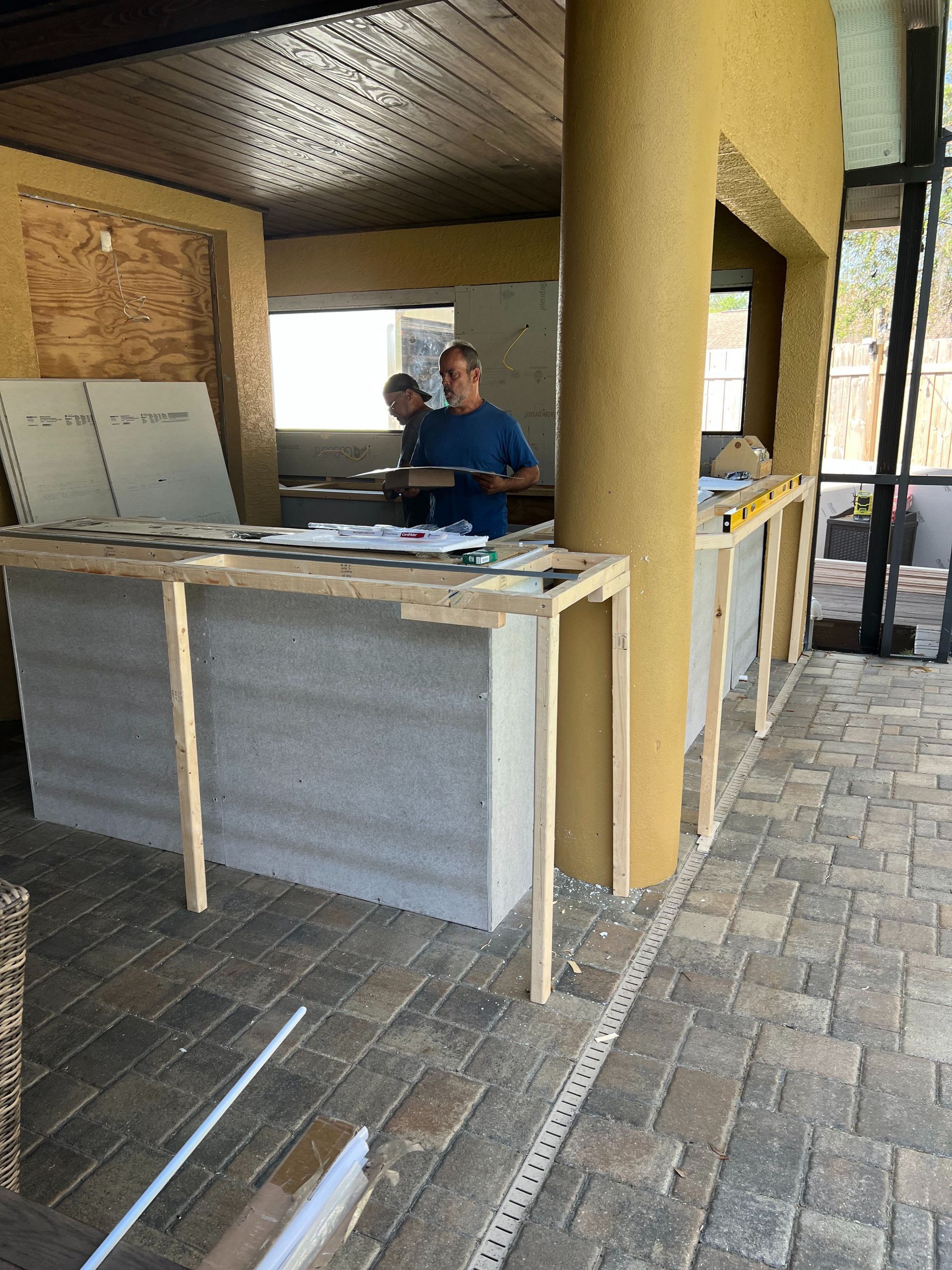 Two people working on a construction project in an outdoor kitchen area with a partially finished bar.