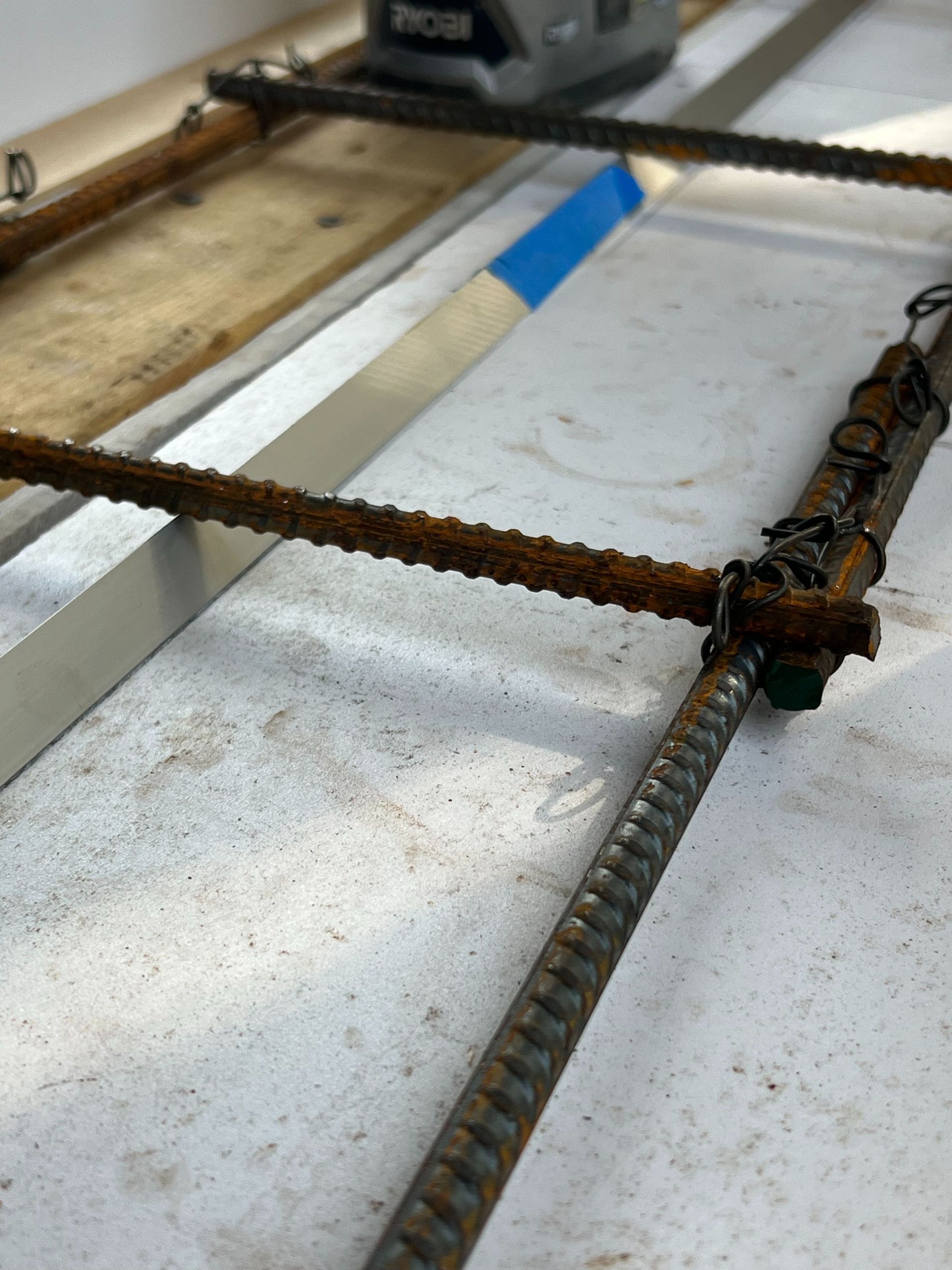 Rebar grid wired together for concrete reinforcement on a flat white surface.