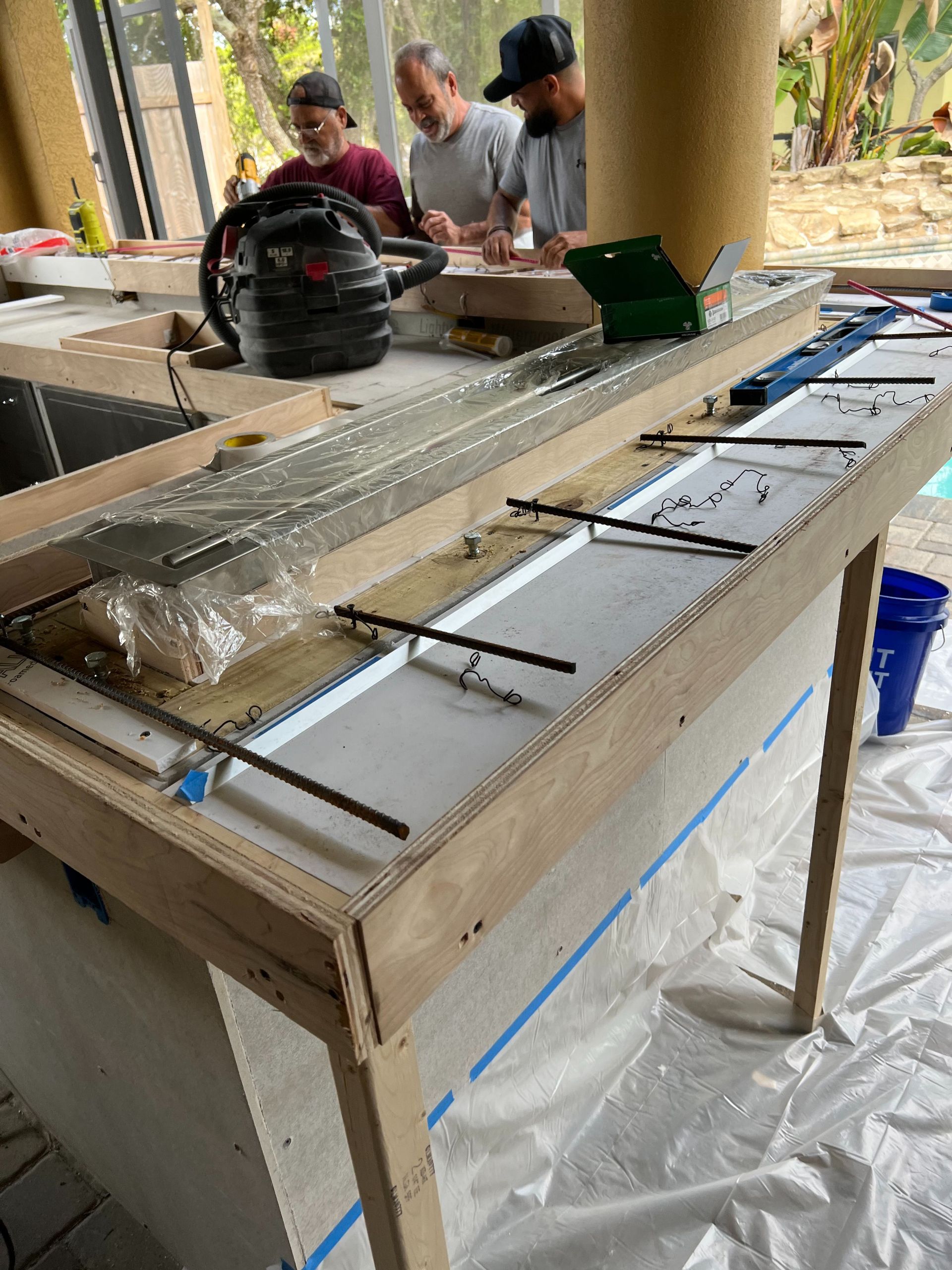 Three people work on constructing a wooden countertop form for a concrete pour in an outdoor patio area.
