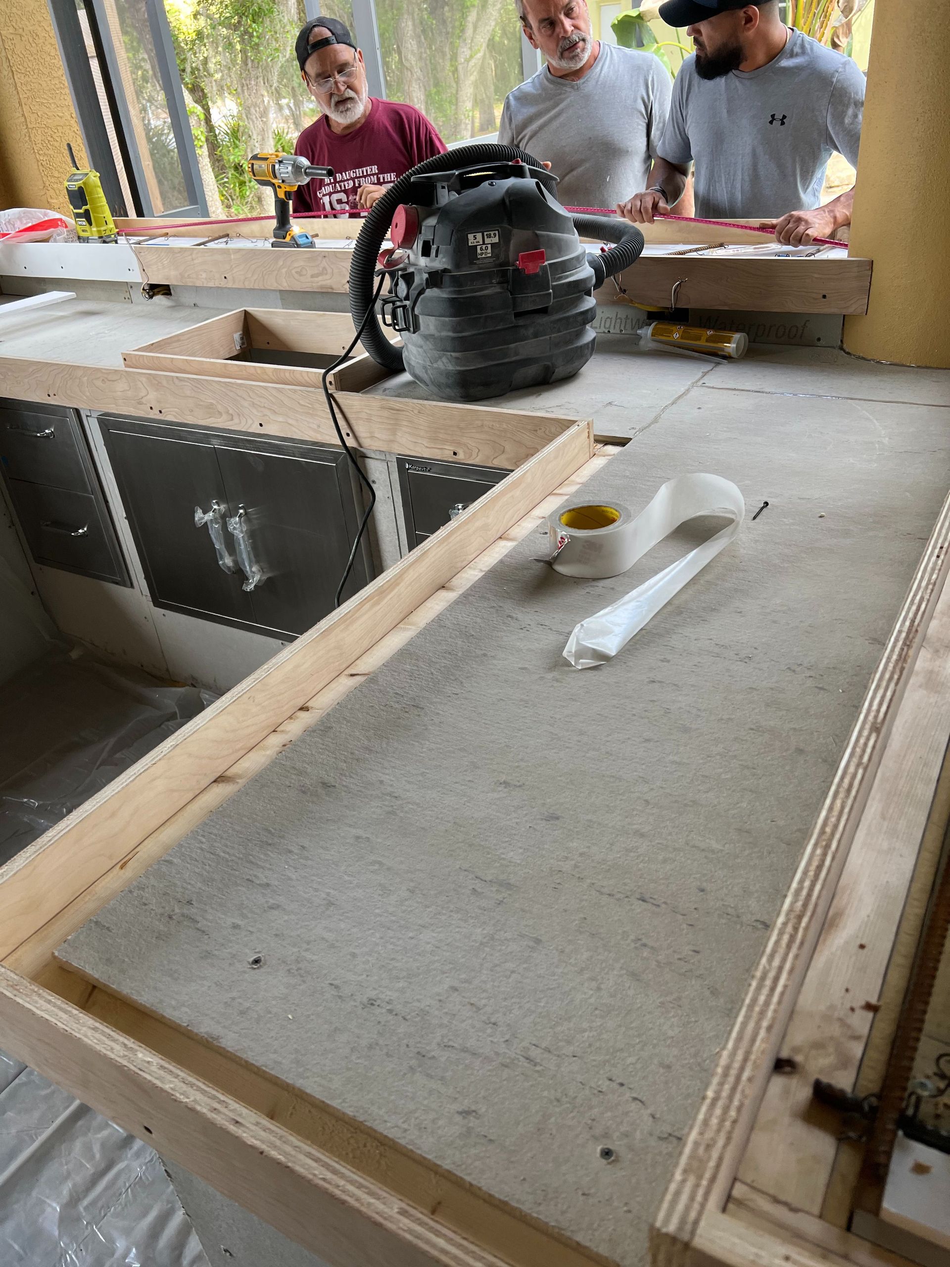 Three people working on a construction site, assembling a wooden counter frame with a cement board countertop surface.