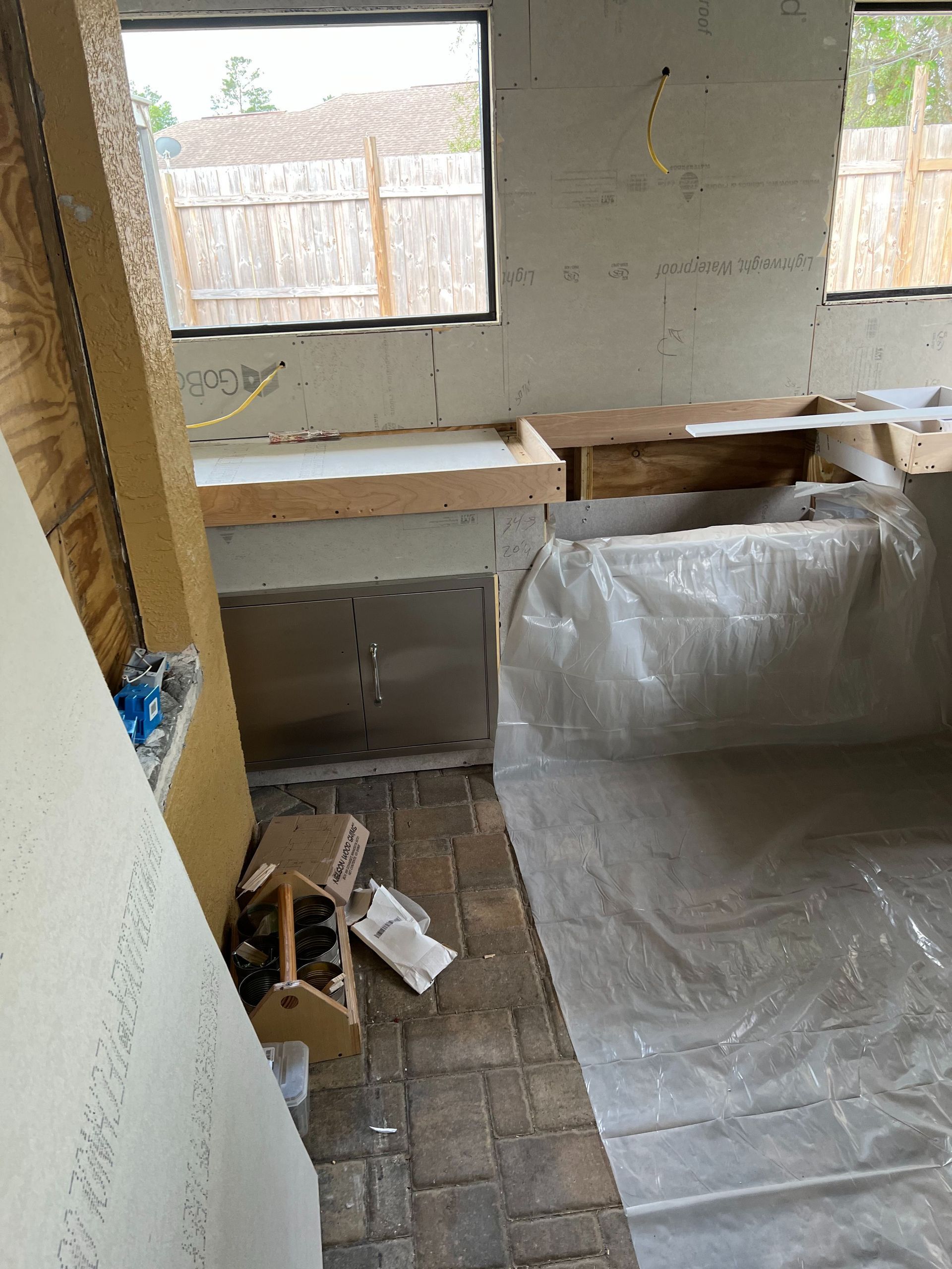 An unfinished indoor space with brick flooring, a partially built countertop, and a protective plastic sheet on the floor.