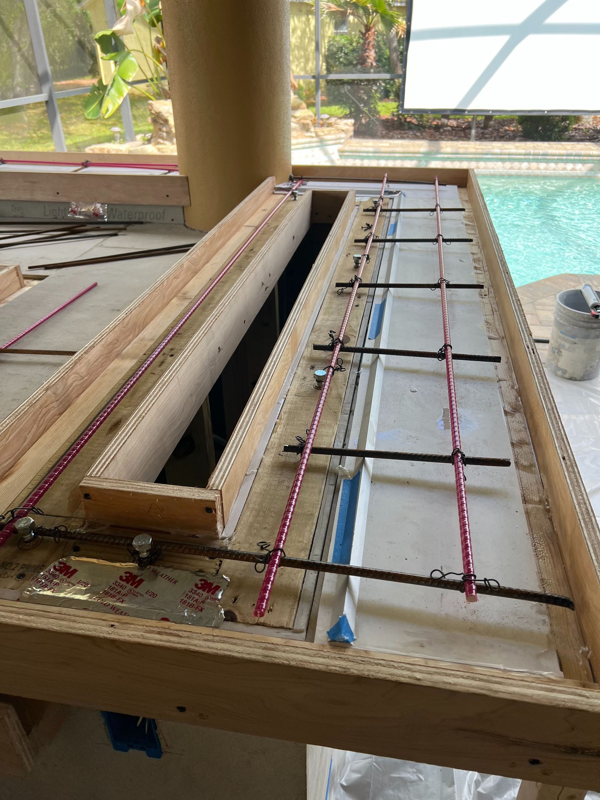 Wooden formwork for a concrete countertop installation, featuring rebar reinforcement and blue painter's tape on a patio.
