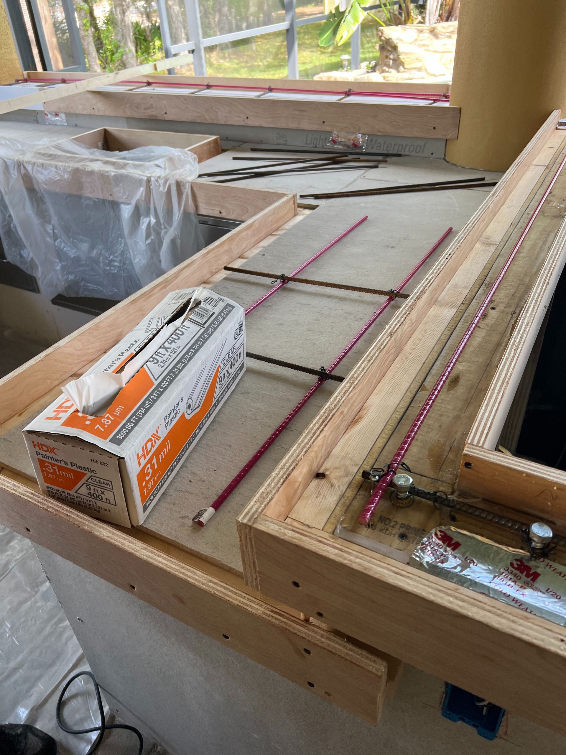Wooden forms for pouring a concrete countertop, with metal reinforcement bars and a box of supplies on a worksite.