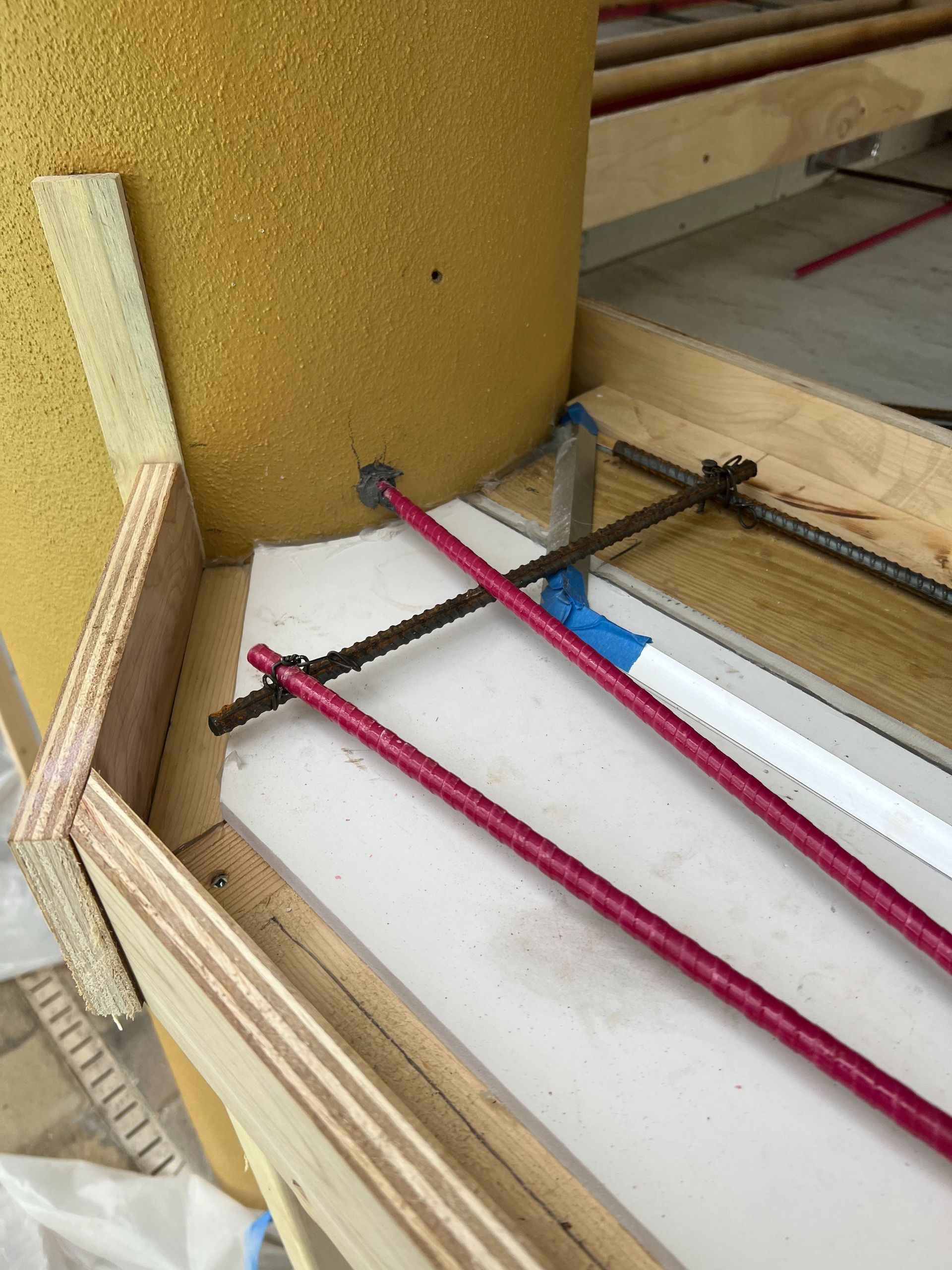 Construction site showing pink rebar dowels inserted into a yellow column base near wooden formwork.
