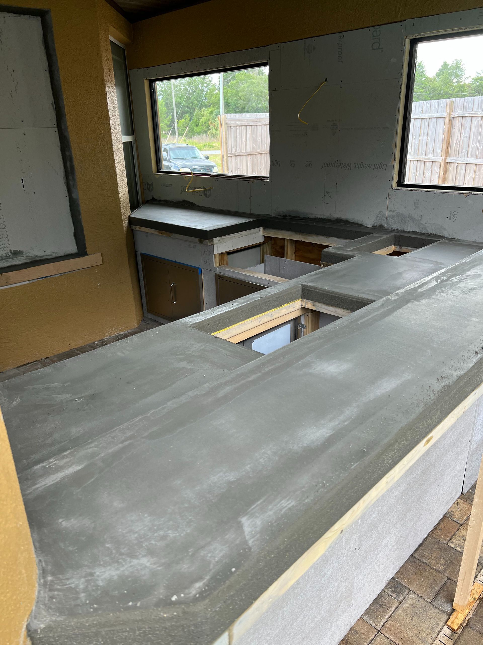 An outdoor kitchen under construction featuring smooth, newly poured concrete countertops set against gray walls.