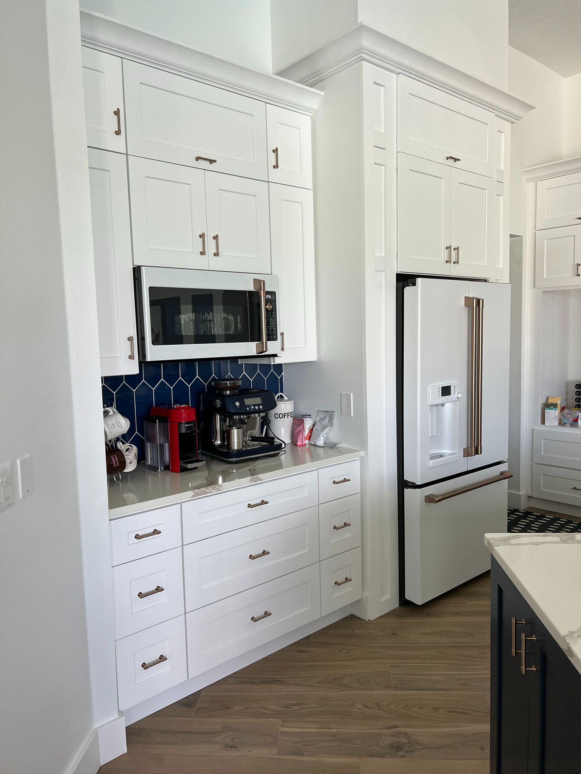White kitchen cabinetry with a built-in microwave, blue tiled backsplash, coffee maker, and stainless steel refrigerator.