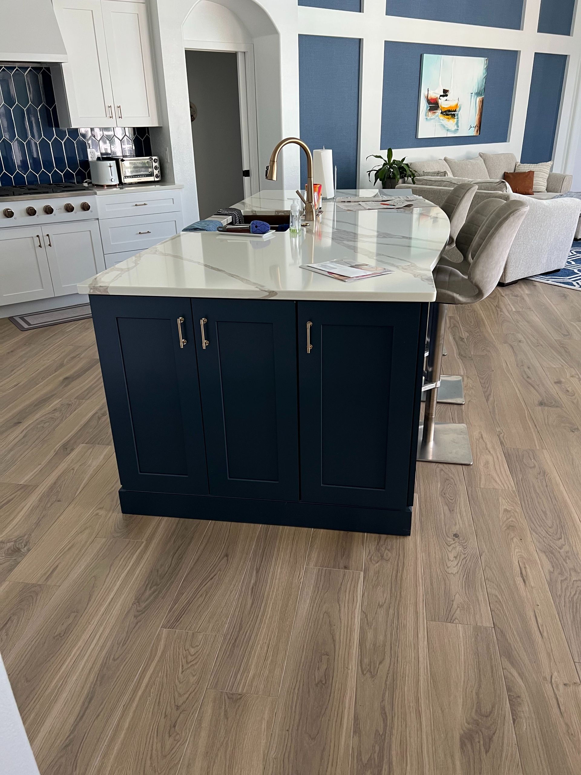 A navy blue kitchen island with a white marble countertop sits on light wood flooring in a modern, open-concept home.