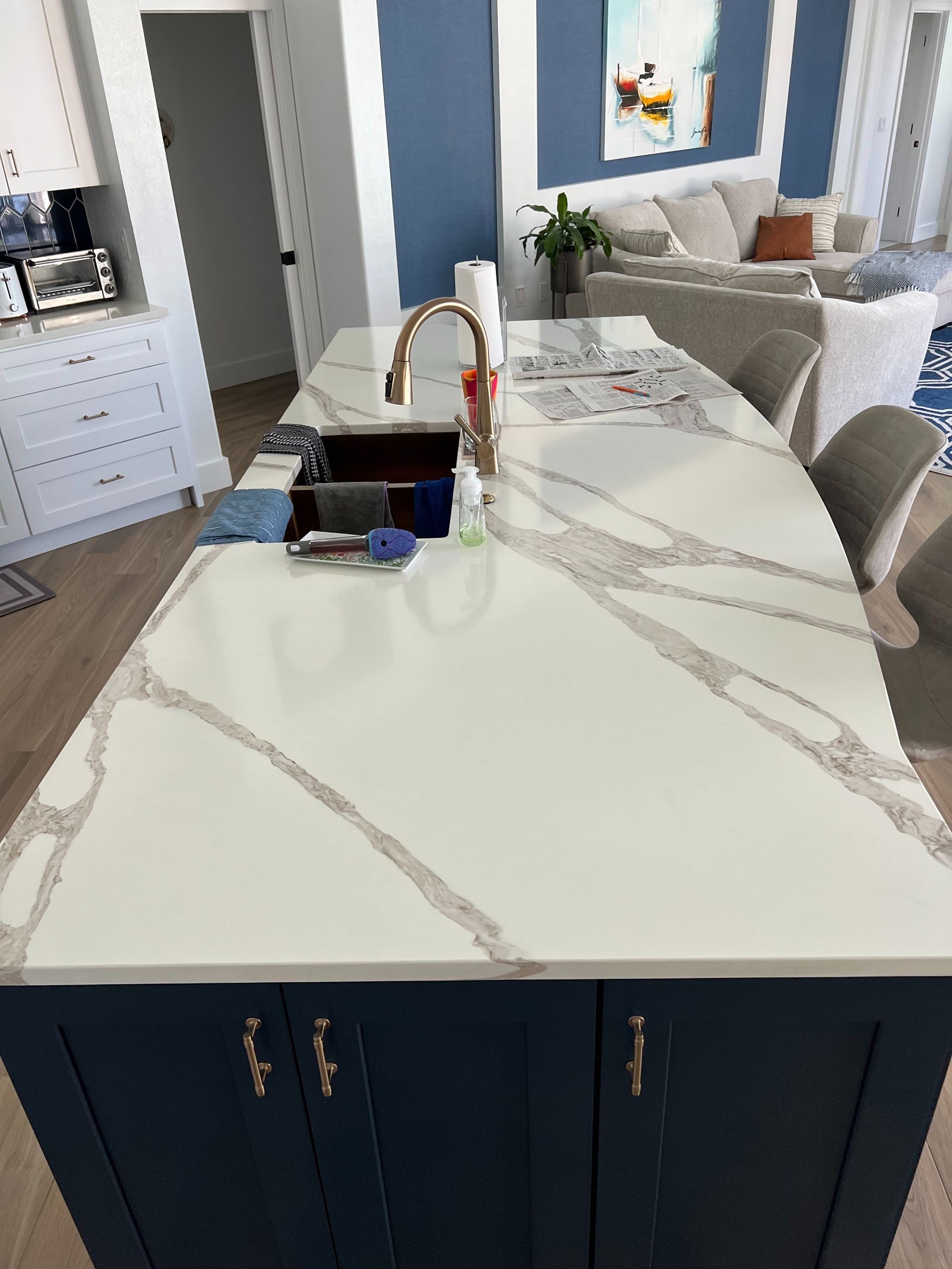 A navy blue kitchen island with a white marble-look quartz countertop, a sink, and a gold faucet in a modern home.