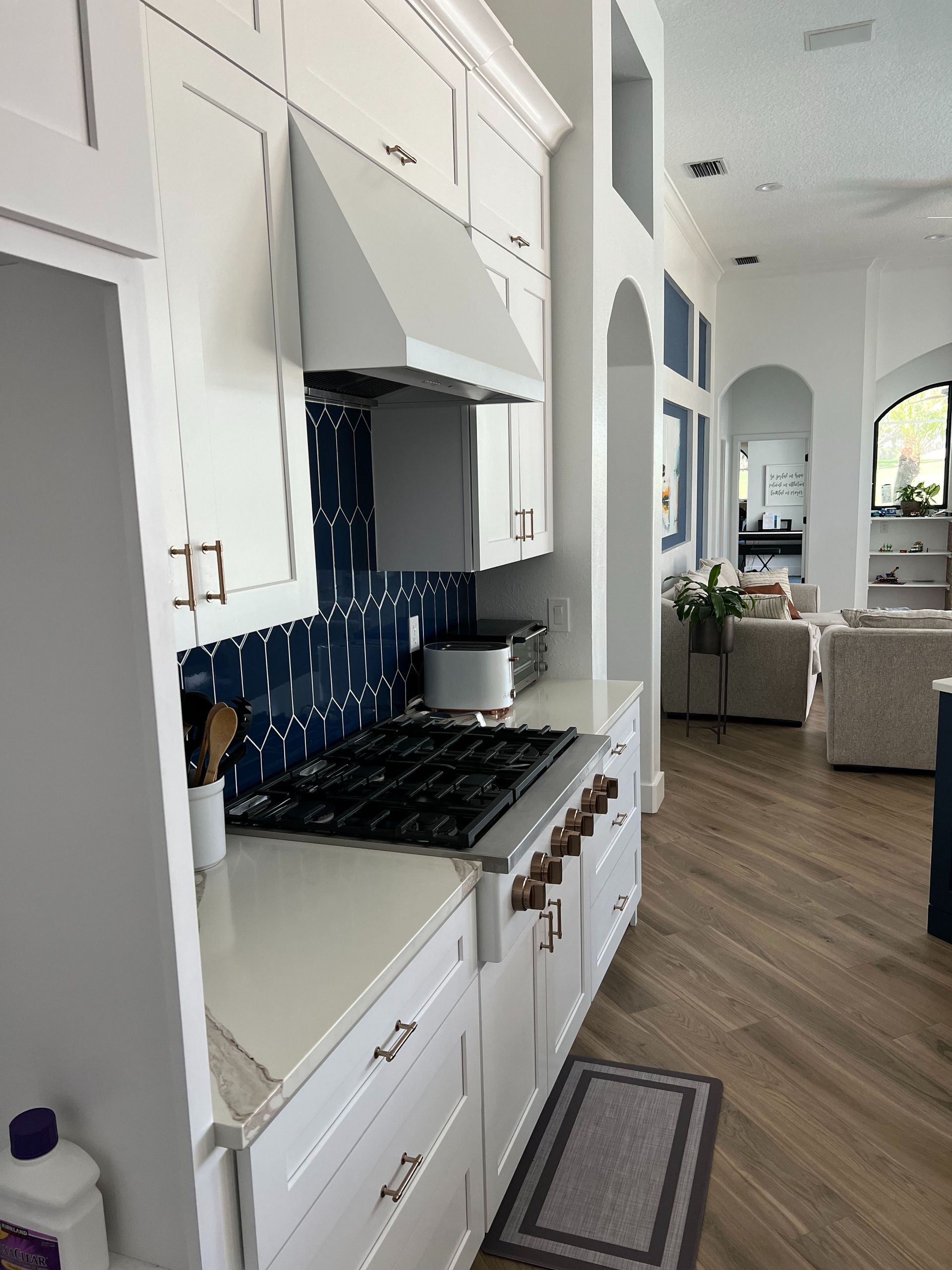 A modern kitchen featuring white cabinets, a navy blue patterned backsplash, a gas range, and wood-look flooring.