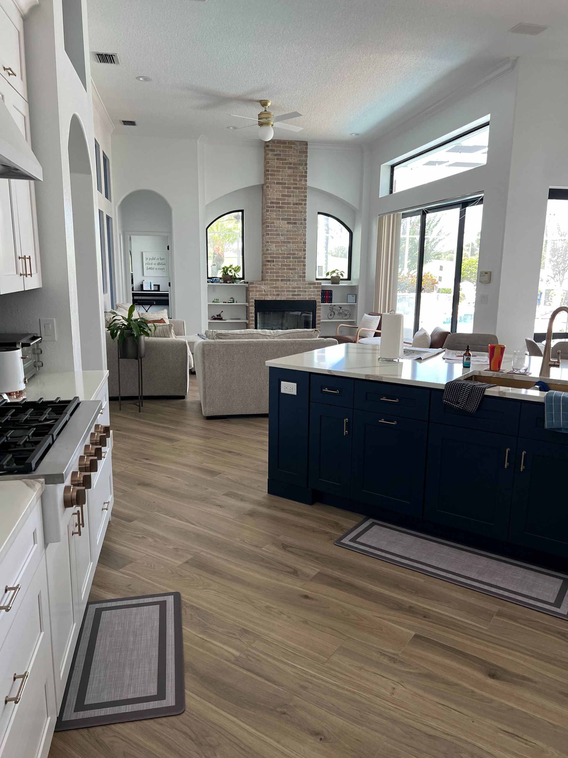 Open-concept kitchen with dark blue cabinets, white countertops, and light wood floors, leading to a bright living area.