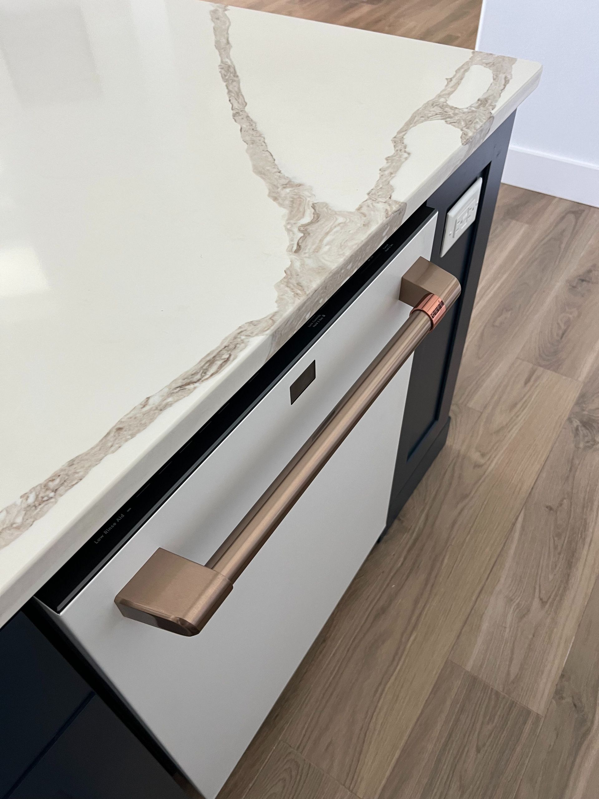 A high-angle view of a white kitchen drawer with a copper handle, set into a dark cabinet with a white marble countertop.