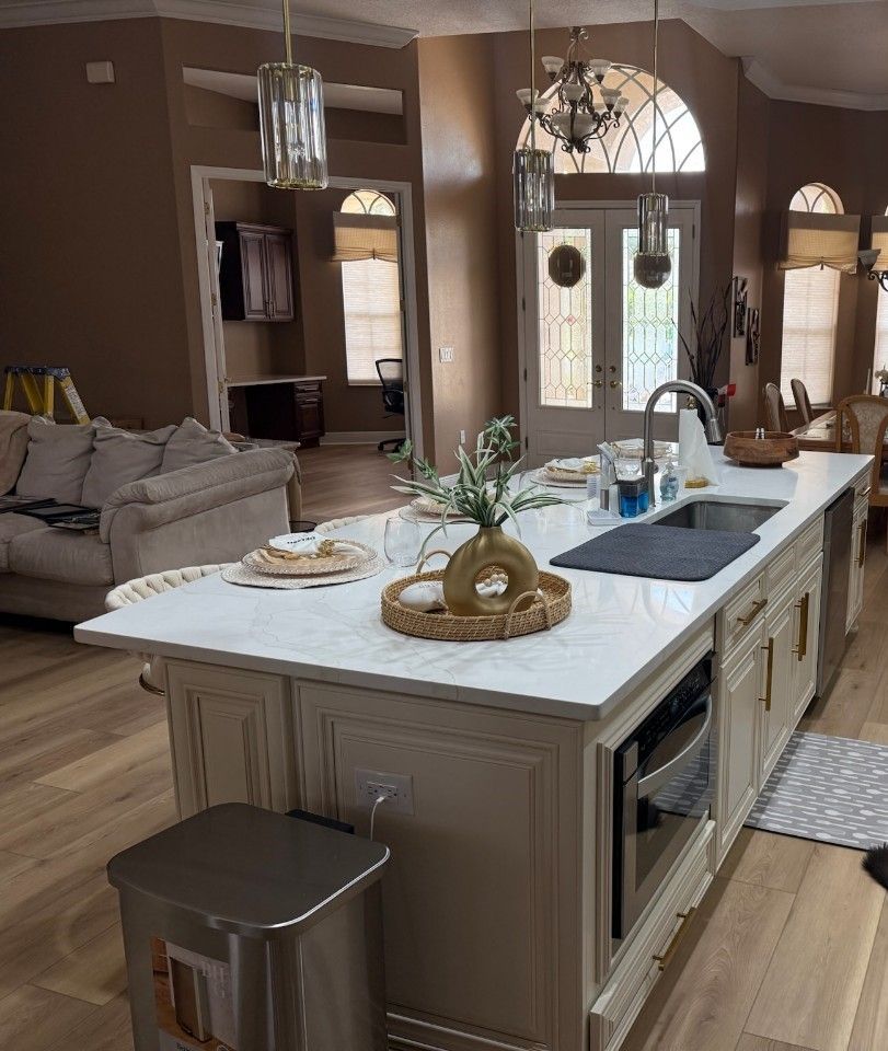 A kitchen island with a white marble countertop, a sink, and decorative vase, set in an open-concept, modern home interior.