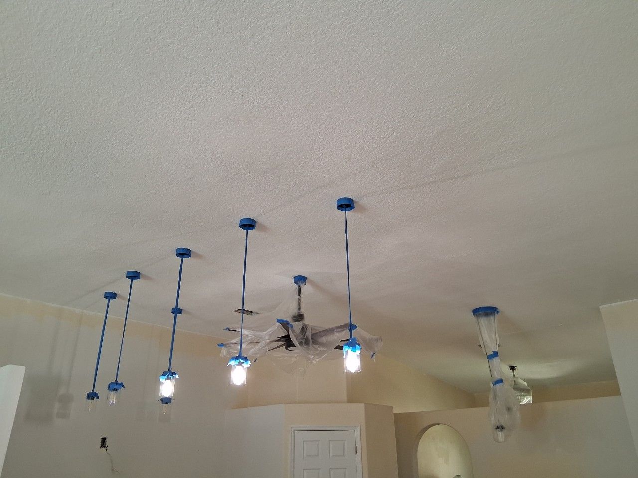 Several pendant lights and a ceiling fan are covered in blue painter's tape and plastic to protect them during painting.
