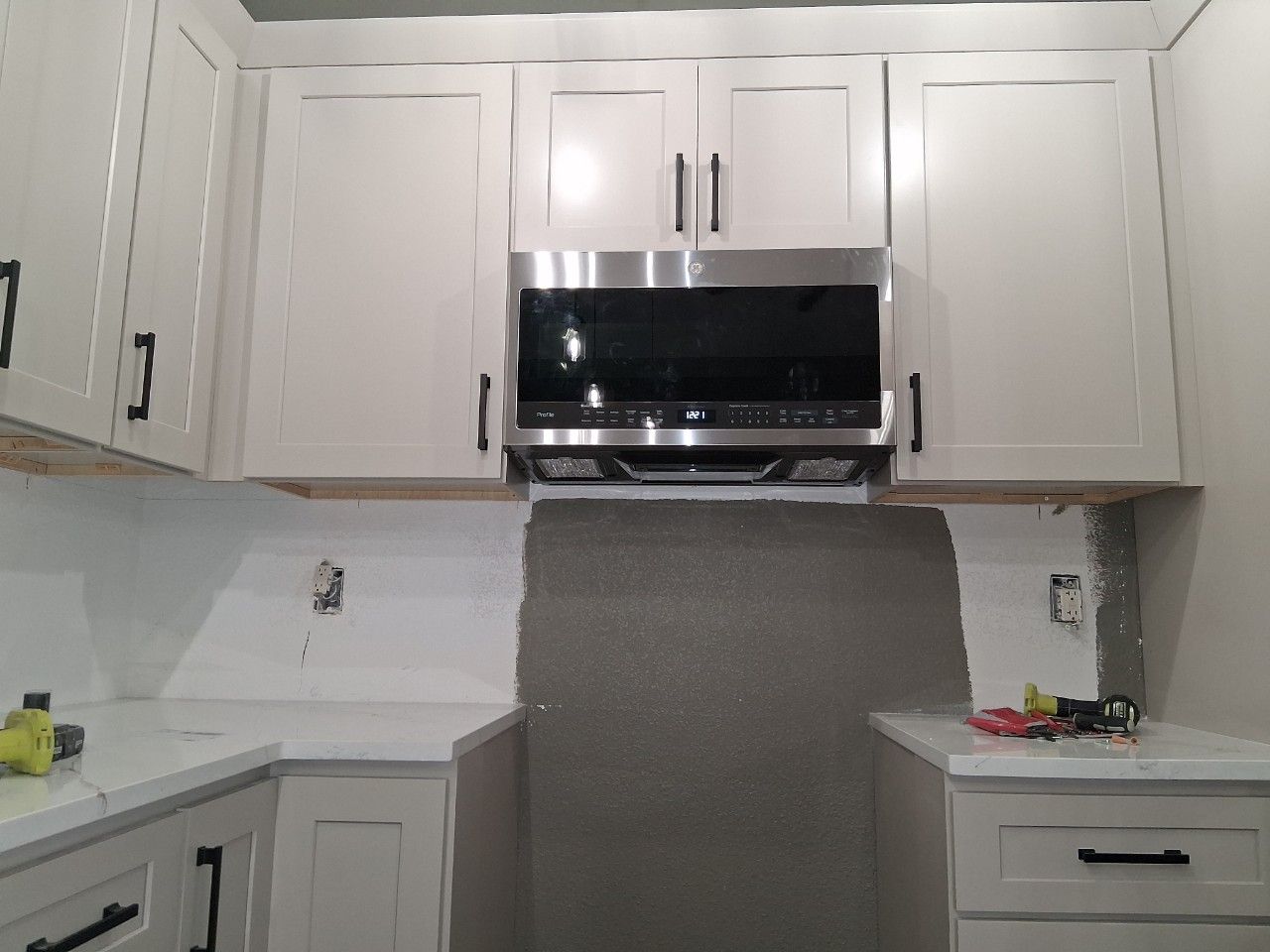 A kitchen under construction featuring white cabinets, a new microwave, white countertops, and unfinished backsplash areas.