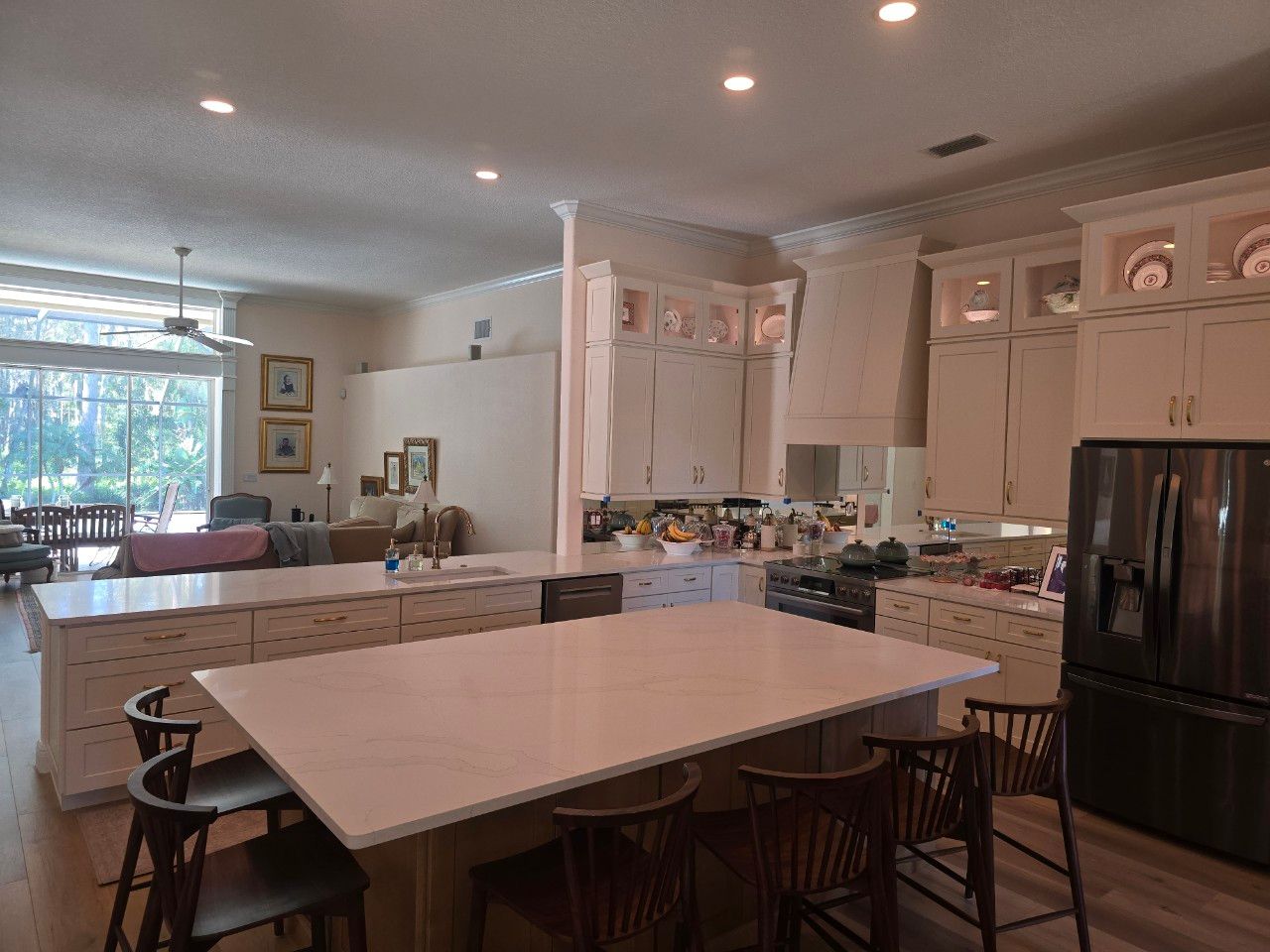 A modern, open-concept kitchen with white cabinetry, a large white island with barstools, and a black refrigerator.