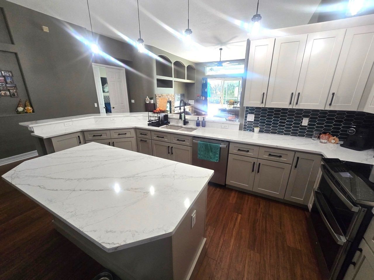 A spacious kitchen featuring a large white quartz island, and a black herringbone backsplash.
