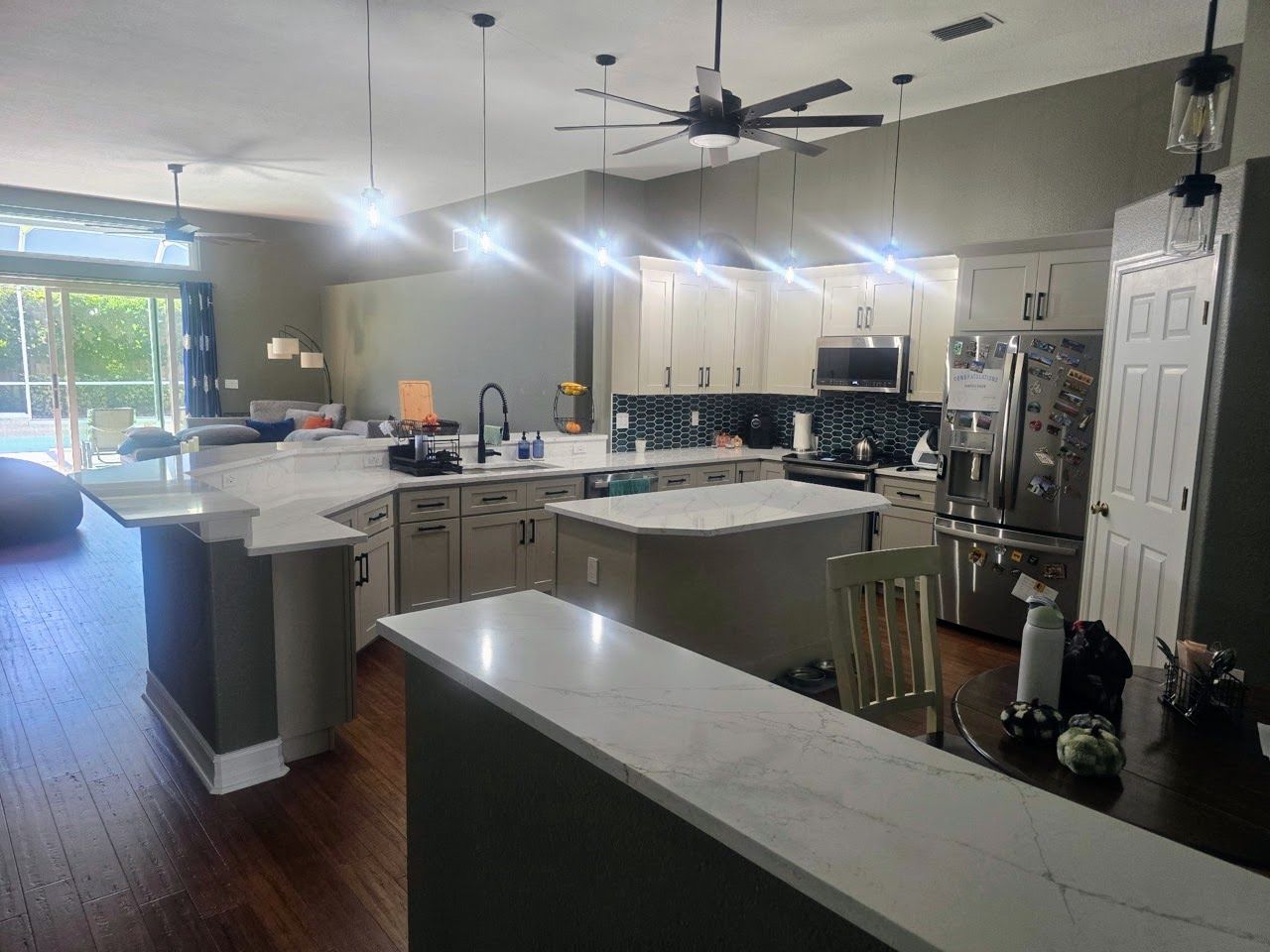 An open-concept kitchen featuring light-colored cabinets, marble-look countertops, an island, and dark wood flooring.