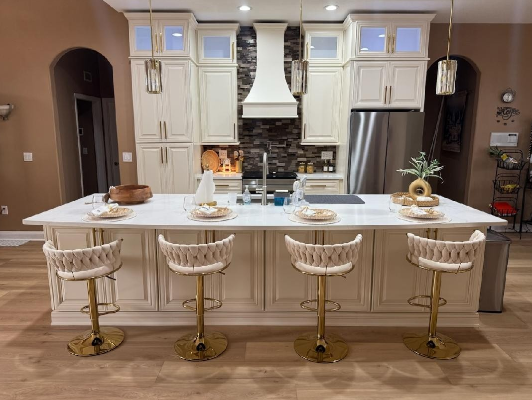 Kitchen island with four beige woven stools, white countertops, and cabinets against a dark stone backsplash.