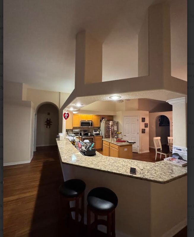 A kitchen with wood cabinets, granite countertops, a bar with two stools, and a large architectural soffit overhead.