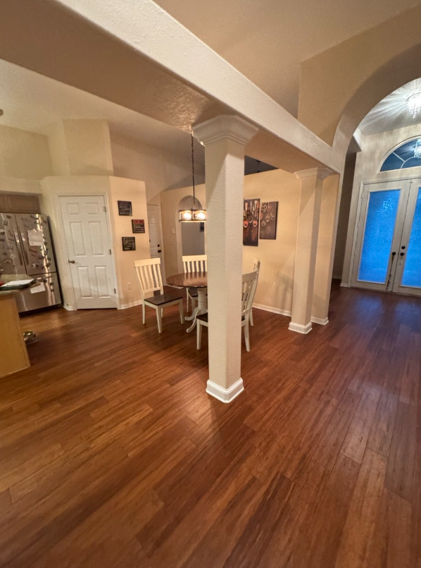 A dining area with a wood table and chairs sits in an open-plan home featuring hardwood floors and arched doorways.