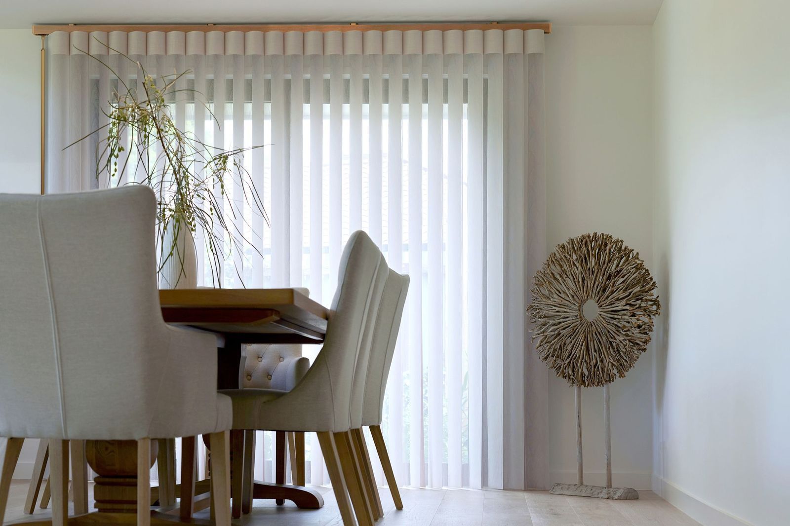 Dining area with upholstered chairs around a table, vertical blinds covering a window, and a decorative sculpture.