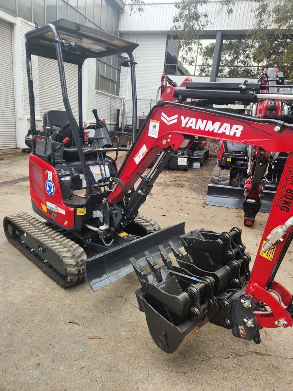 A red yanmar excavator is parked in front of a building.