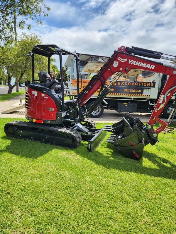 A red and black excavator is parked on a lush green field.
