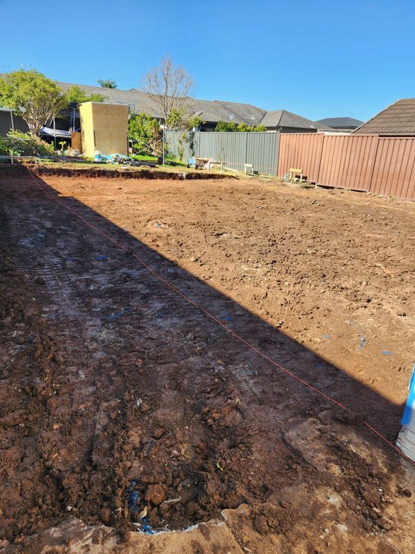 A dirt field with a fence in the background and a house in the background.