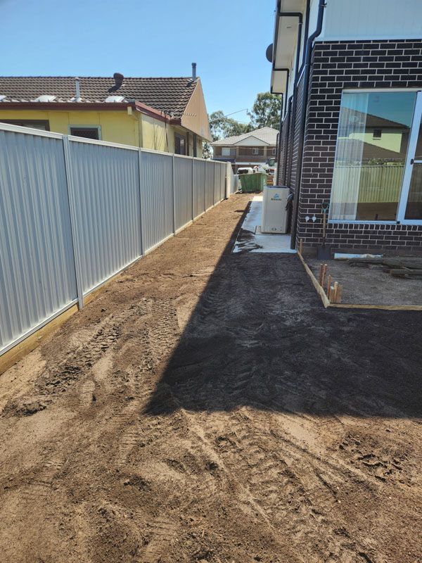 A dirt path leading to a brick house with a fence.