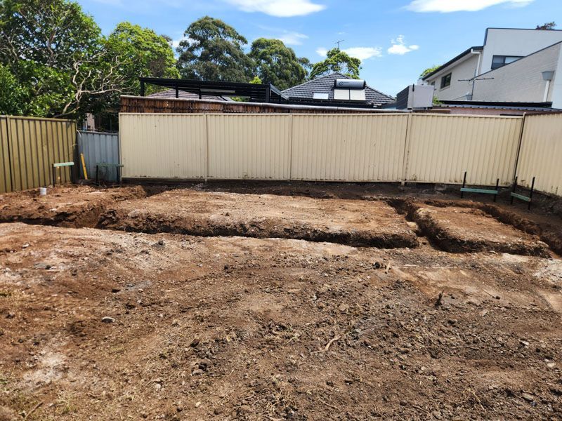 A dirt field with a fence in the background and a house in the background.