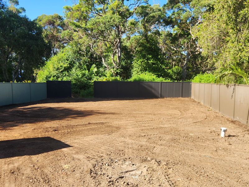 A dirt field with a fence and trees in the background
