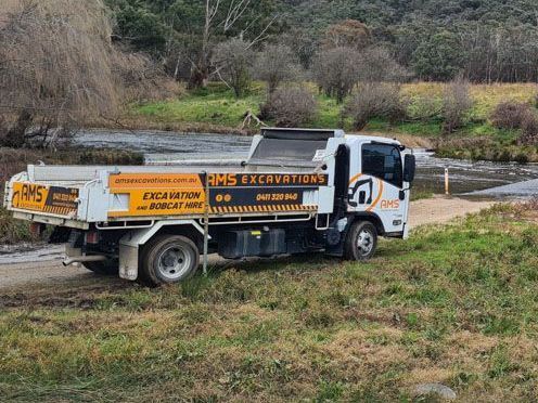 A dump truck is parked on the side of a dirt road next to a river.
