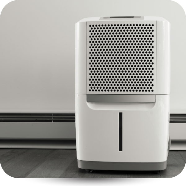 White dehumidifier standing on a gray floor against a wall with baseboard heater