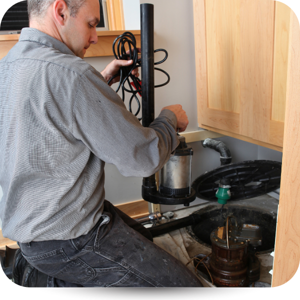 Man repairing a black kitchen sink garbage disposal under a wooden cabinet