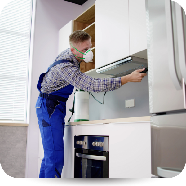 Worker in blue overalls installing a kitchen cabinet while wearing a protective mask
