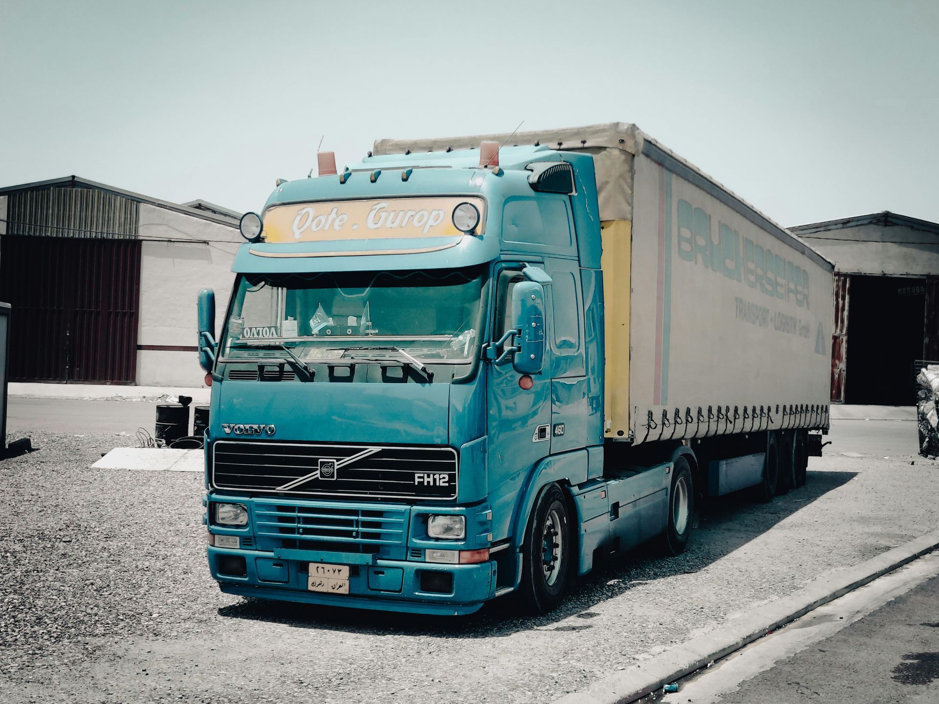 Turquoise vrachtwagen met witte oplegger geparkeerd op een industrieterrein.