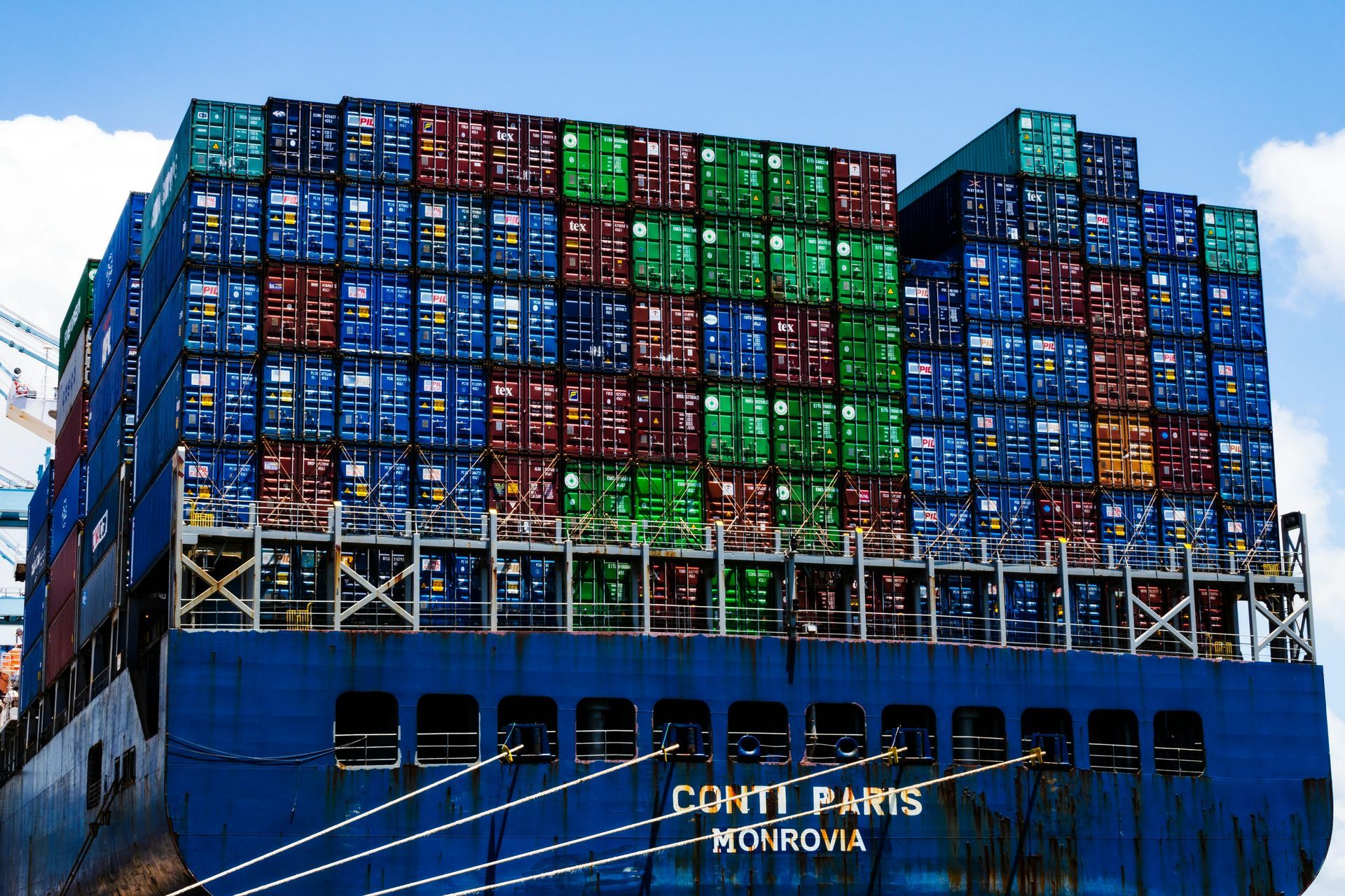Een volgeladen containerschip, hoog opgestapeld met kleurrijke zeecontainers, vaart over zee.