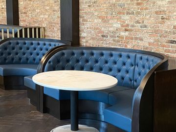 Blue tufted booths and a round table in a brick-walled café interior Blue tufted booths and a round table in a brick-walled café interior