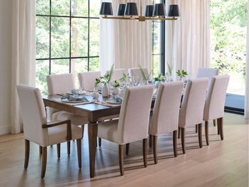 Modern dining room with a long table, beige chairs, and large windows overlooking greenery Modern dining room with a long table, beige chairs, and large windows overlooking greenery