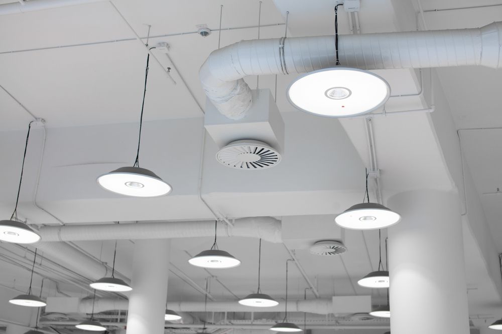 A ceiling with a lot of pipes and lights hanging from it.
