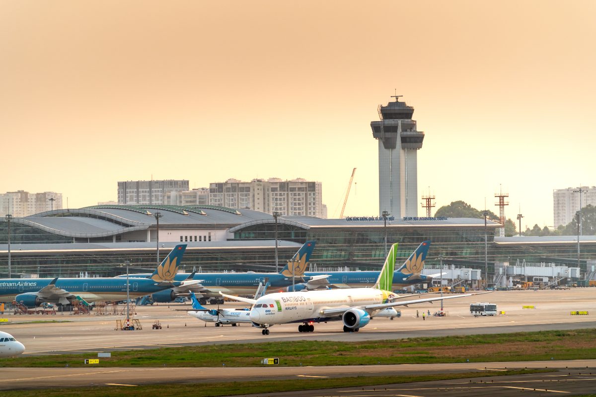 Airplanes on an airport tarmac with a control tower and terminal buildings at sunset