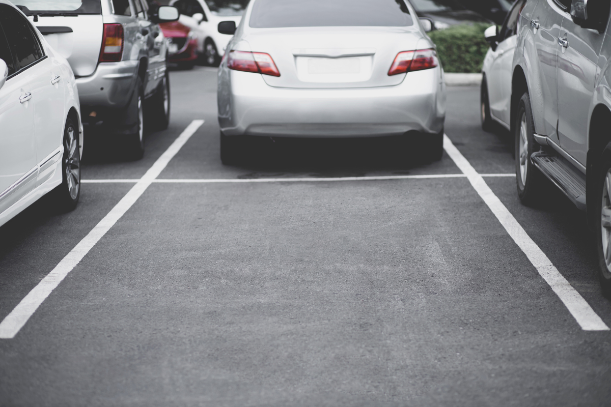 Cars parked in marked parking spaces in a lot, with a white sedan centered