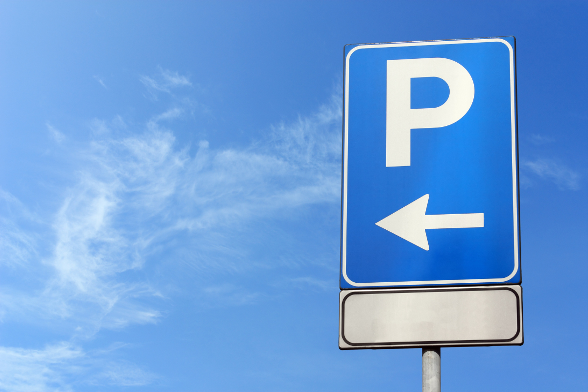 Blue parking sign with a left-pointing arrow against a clear sky