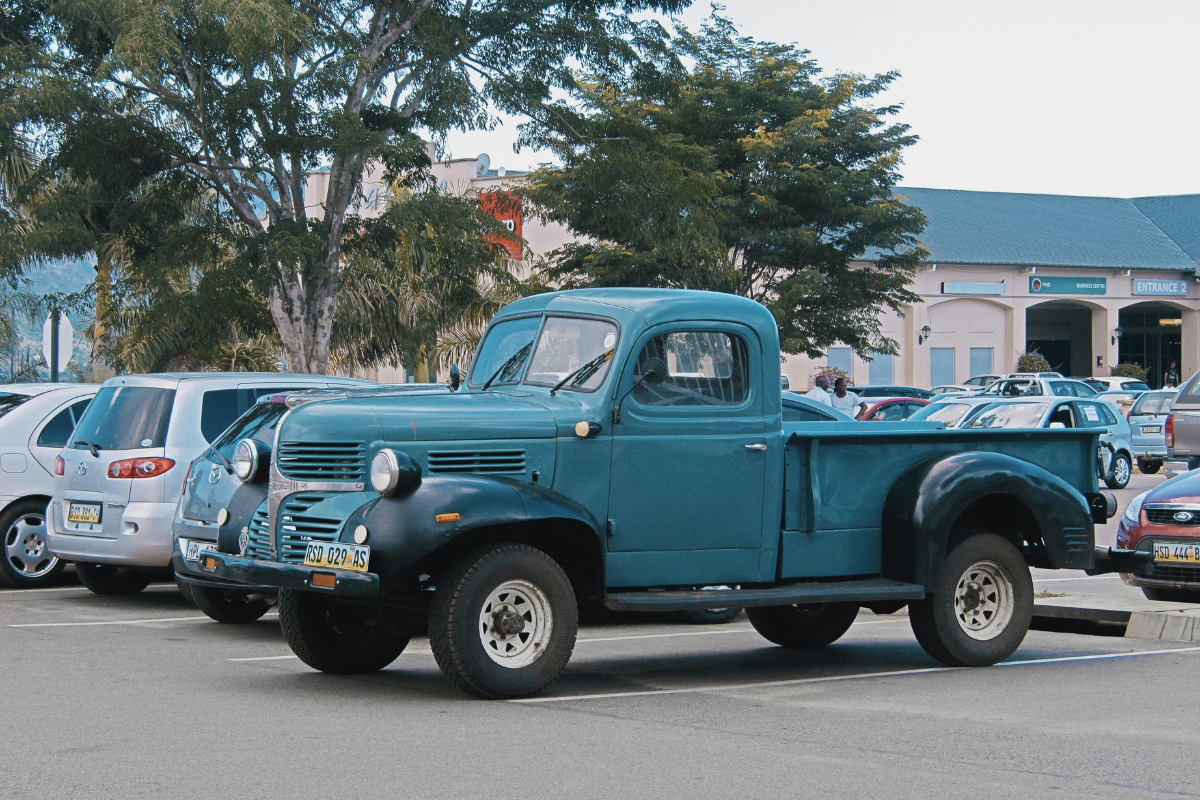 Vintage teal pickup truck parked in a lot with other cars and trees in the background