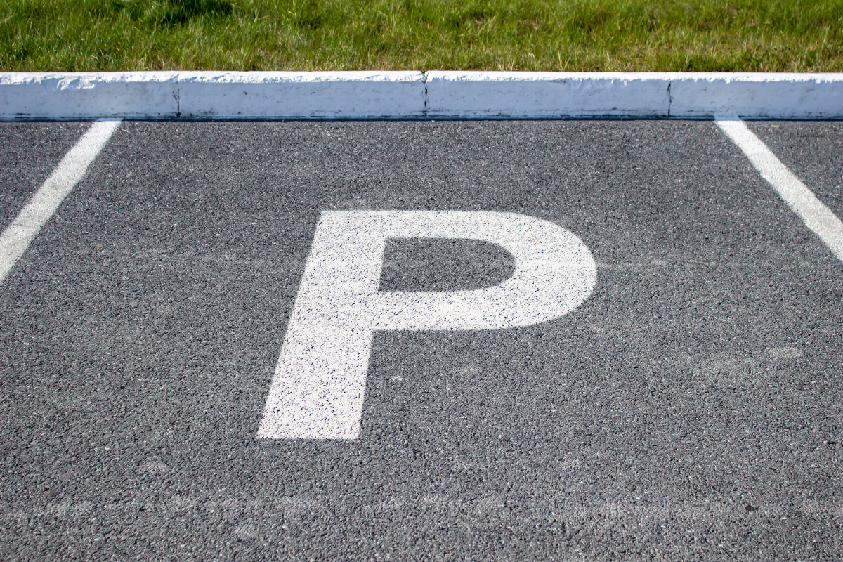White parking space with a large painted “P” on gray asphalt next to a curb