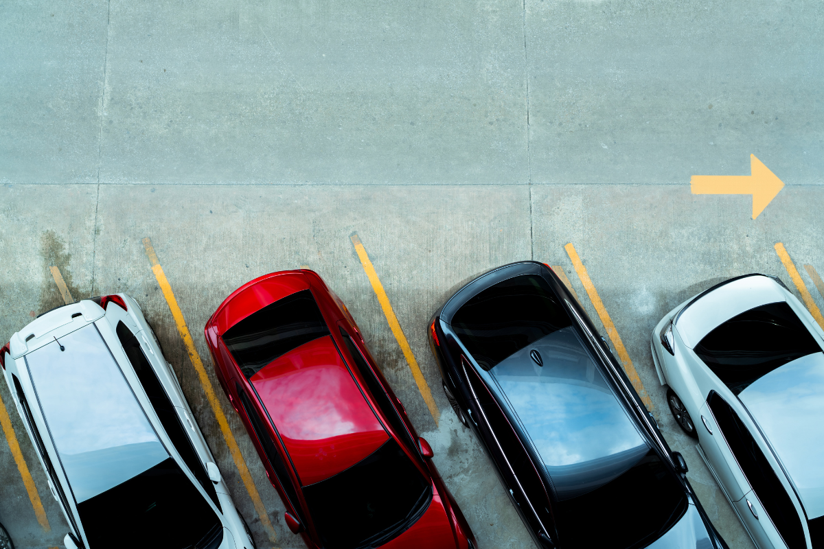 Overhead view of parked cars in marked spaces, with a yellow arrow pointing right