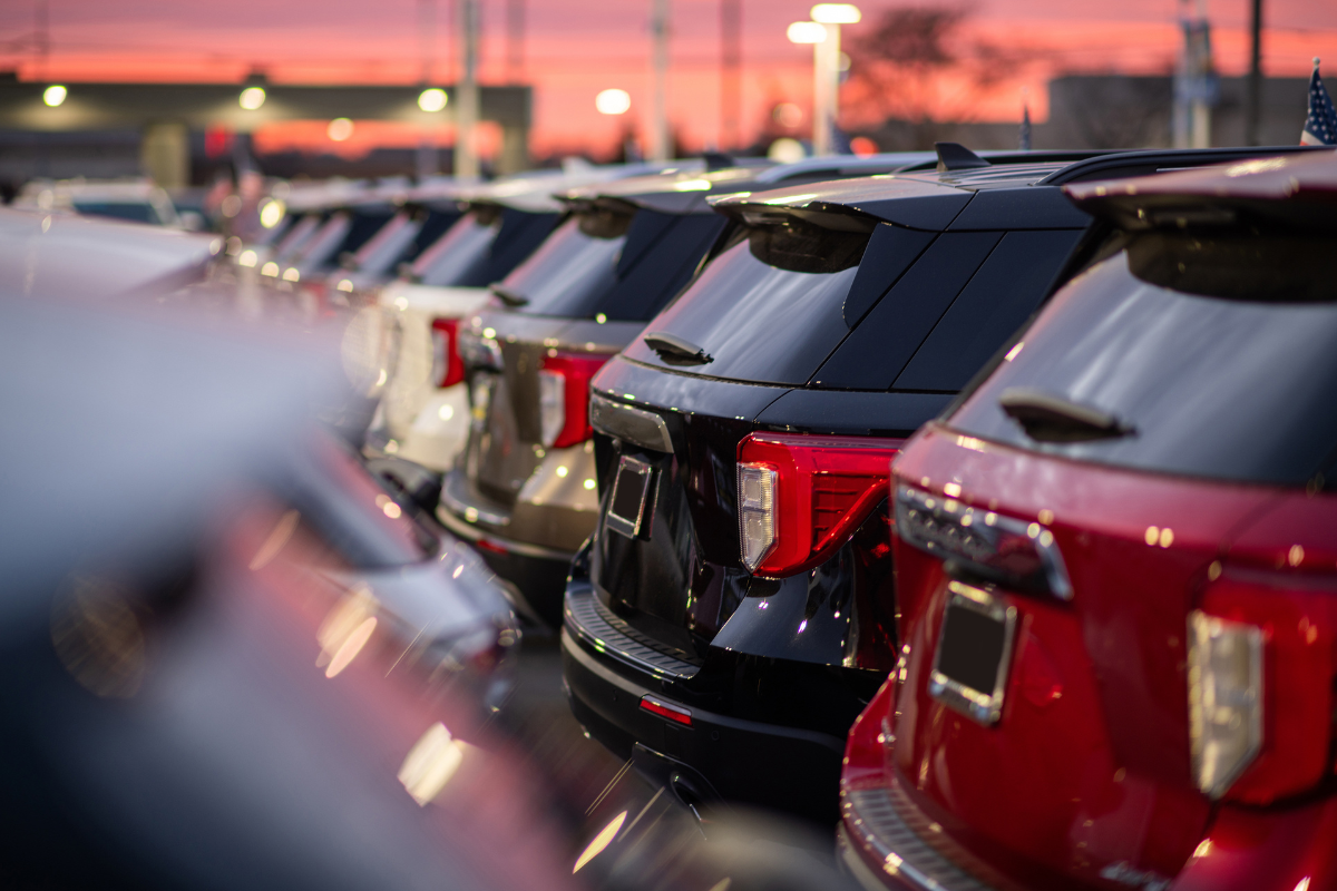 Row of parked cars in a lot at sunset, with red and black vehicles in the foreground